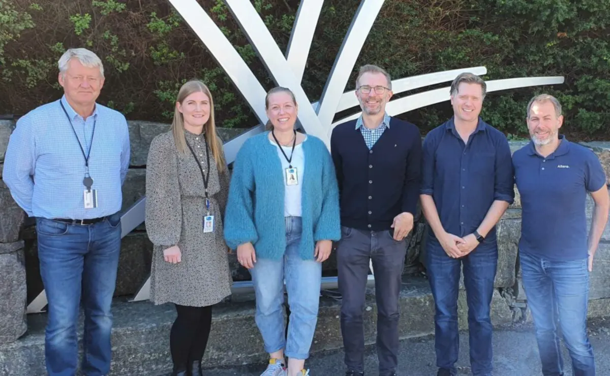 Six employees standing in front of a metal sculpture outdoors