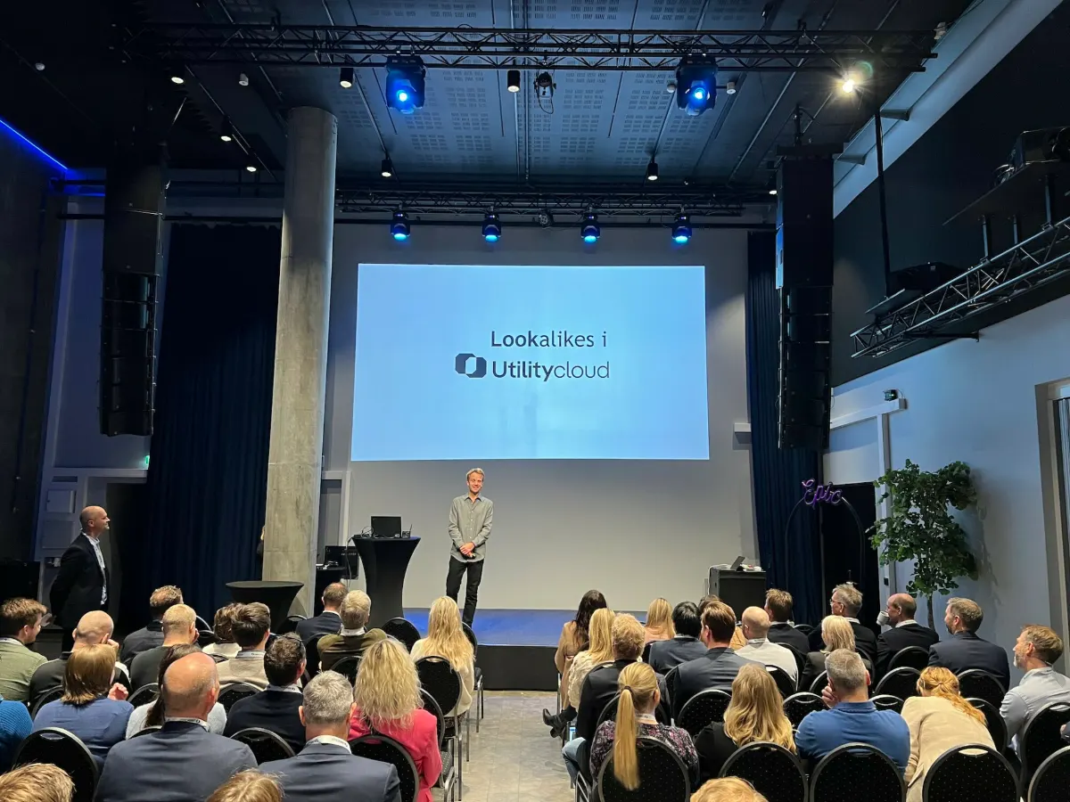 Presenter standing on stage in front of a screen reading 'Lookalikes i UtilityCloud'