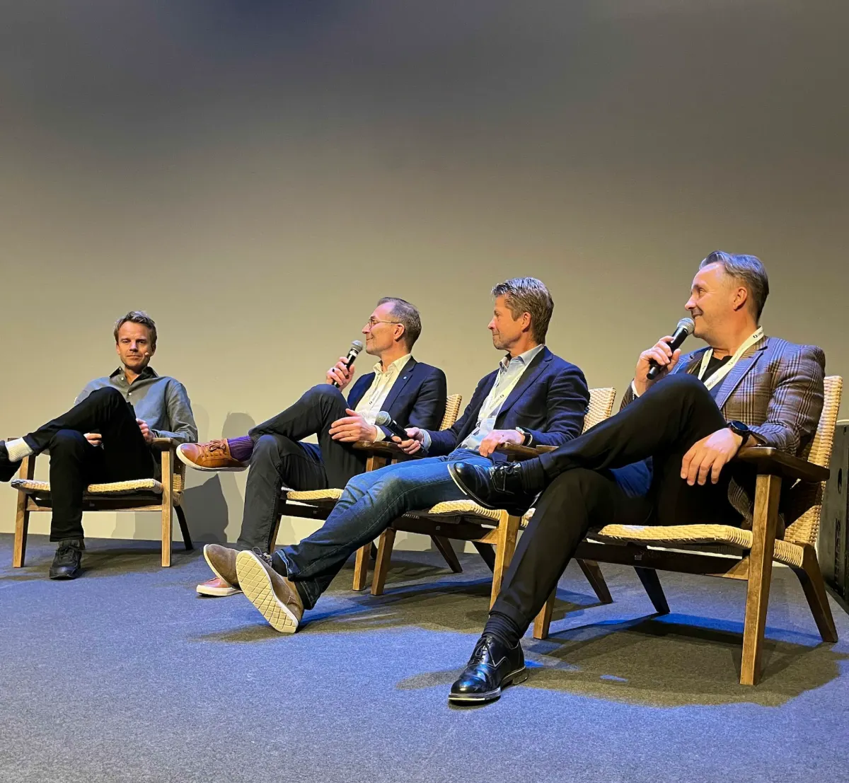 Four panelists seated on stage with microphones, speaking to an audience