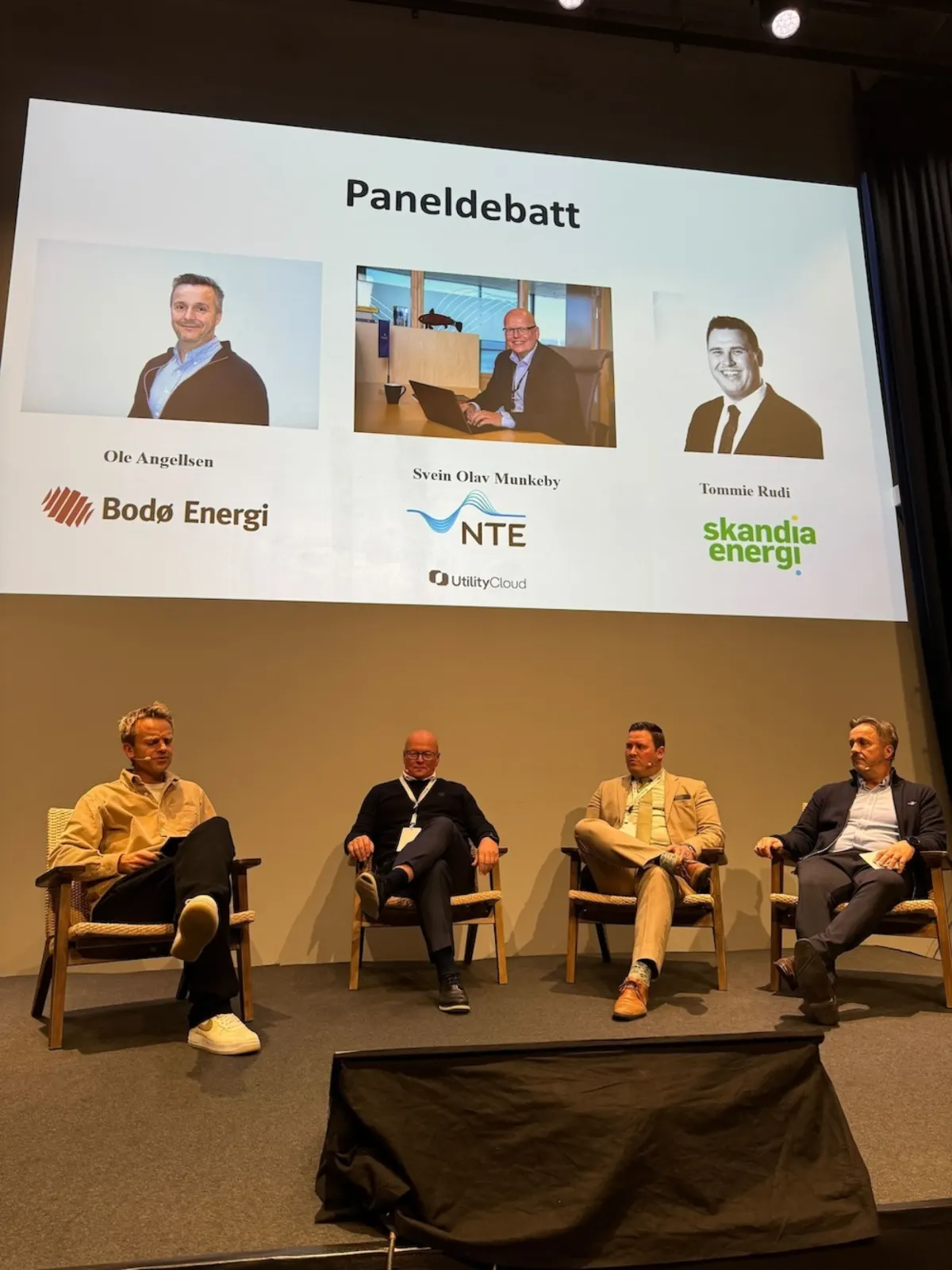 Four panelists on stage under a 'Paneldebatt' slide showing their photos and company logos
