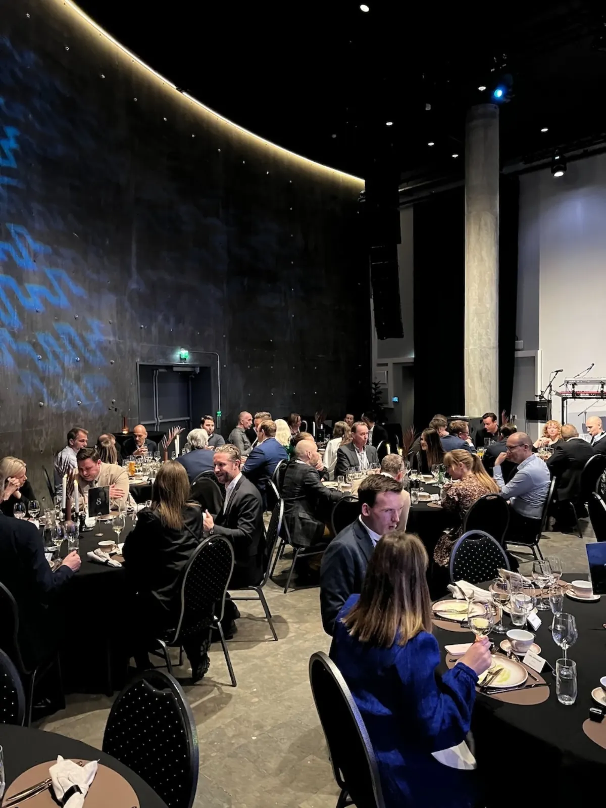 Evening conference dinner with guests seated at round tables in a dark hall