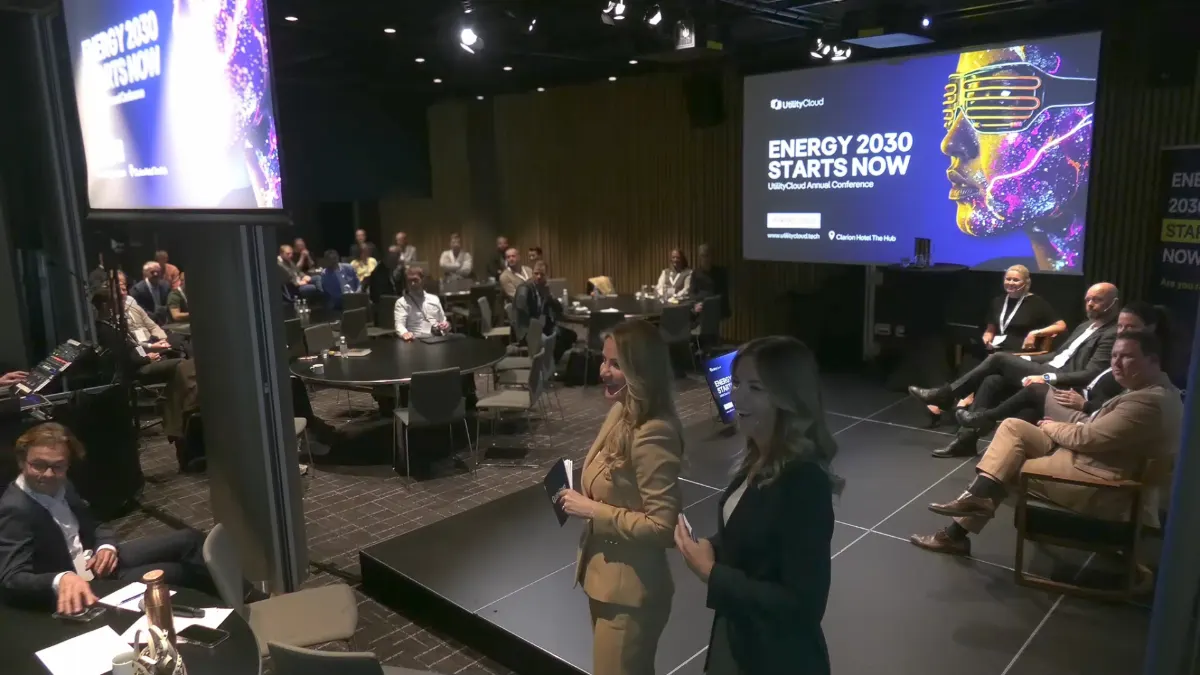 Two hosts on stage at the Energy 2030 conference, screen reading 'Energy 2030 Starts Now'